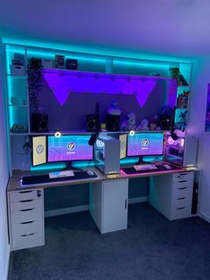 two computer monitors sitting on top of a desk in front of a purple and blue wall