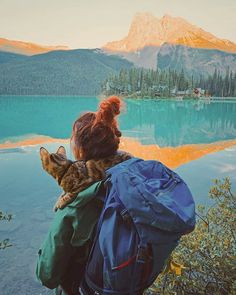 a woman with a cat on her back looking at the water and mountains in the distance