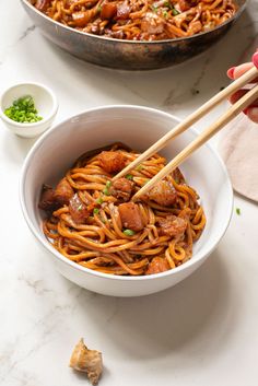 someone is holding chopsticks in a bowl of noodles with meat and vegetables on the side