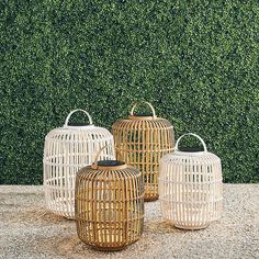 three white wicker lanterns sitting on top of a cement ground next to a green hedge