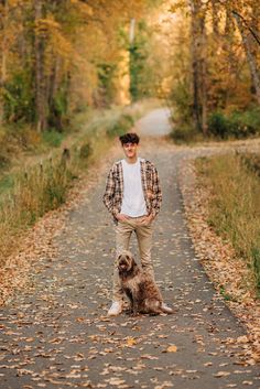 a man standing next to a dog on a dirt road surrounded by trees and leaves