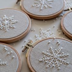 embroidered snowflakes are displayed on wooden hooplets with bead trimming