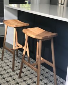 two wooden stools sitting on top of a tiled floor next to a kitchen counter