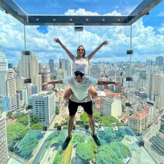 a man and woman standing on top of a glass floor in the middle of a city