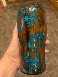 a hand holding a wooden tumbler with blue glitters on it's side