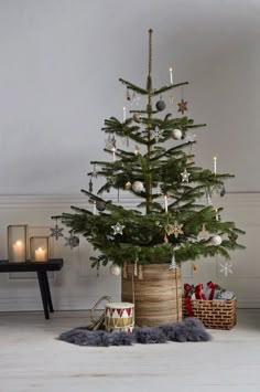 a small christmas tree in a wooden basket with candles and ornaments around it on the floor