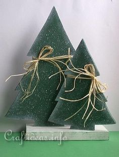 two small christmas trees are sitting on a green table top with twine ribbons tied around them