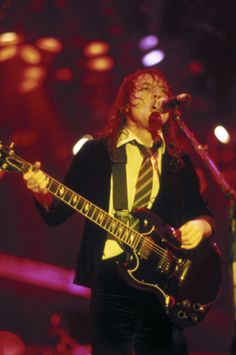 a man with long red hair is playing an electric guitar and singing into a microphone