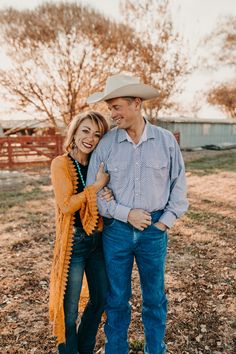 a man and woman are standing together in the grass, smiling at each other while wearing cowboy hats