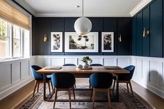 a dining room table with blue chairs and pictures on the wall in front of it