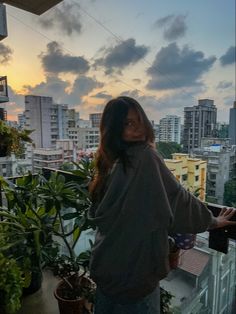 a woman standing on top of a balcony next to a potted plant in front of a cityscape