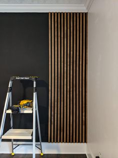 a ladder is standing in front of a black wall with vertical striped drapes on it