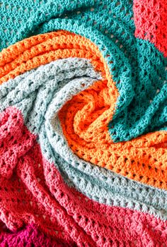 crocheted blanket laying on top of each other with different colored yarns around it