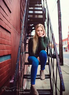 a beautiful young woman sitting on top of a set of stairs next to a red brick building