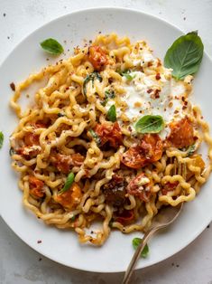 a white plate topped with pasta covered in tomato sauce and parmesan cheese next to a fork