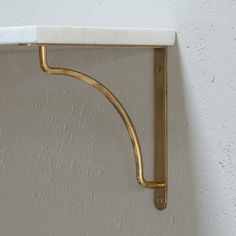 a gold shelf with a white marble top and brass brackets on it's sides