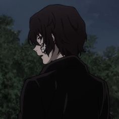 a man with black hair standing in front of trees and looking off into the distance