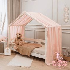 a teddy bear sitting on top of a bed in a room with pink drapes