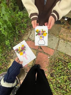 two people holding cards with flowers on them, and one has a card in the shape of a vase