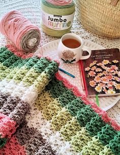 a crocheted blanket on a table next to a cup of coffee and yarn