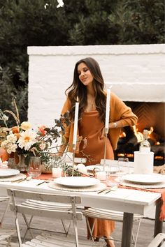 a woman standing next to a table with plates and flowers on it