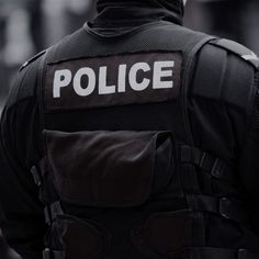 a police officer with his back to the camera, wearing a black jacket and white writing on it