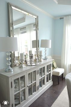 a living room filled with furniture and a large mirror on top of a dresser next to a window