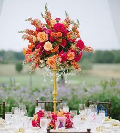 a tall vase filled with lots of colorful flowers on top of a table covered in white linens