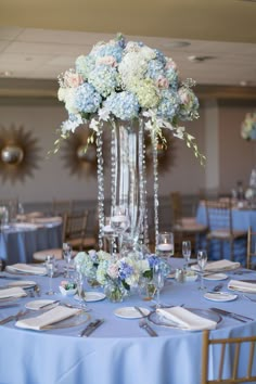 a tall vase filled with white and blue flowers on top of a table covered in silverware