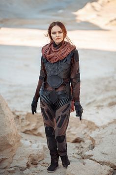 a woman dressed in black and brown standing on rocks