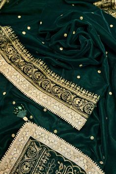 Look stunning in our bottle green designer velvet saree. Made with soft velvet fabric, it features intricate zari embroidery all over, created using a special machine. The lace border is adorned with delicate mirrorwork, and the pallu has tassels hanging from it. Elevate your ethnic wardrobe with this unique and luxurious saree. Color: A shade of bottle green color Technique: An enriching work of zari embroidery with a lace border with mirror work and tassels on the pallu. Fabric: Velvet Festive Velvet Saree, Velvet Saree With Pallu For Wedding, Traditional Gold Velvet Wear, Traditional Dark Green Dupatta With Resham Embroidery, Gold Velvet Traditional Wear, Velvet Saree With Zari Work And Traditional Drape, Bollywood Velvet Saree With Zari Work, Designer Velvet Traditional Wear With Pallu, Designer Gold Velvet Dupatta