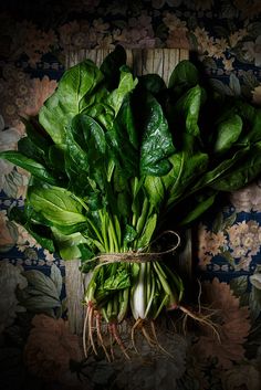 a bunch of green leafy vegetables sitting on top of a wooden table next to a wall