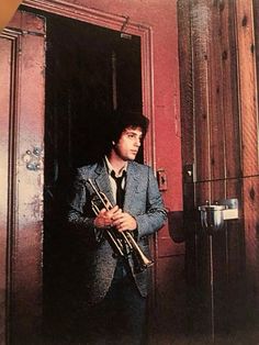 a man in a suit and tie holding a trumpet standing next to an open door