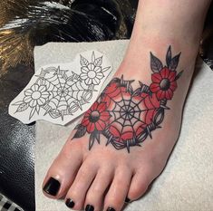 a woman's foot with red flowers and spider web tattoo on the bottom of it