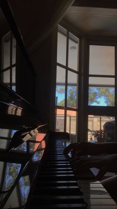 someone is playing the piano in front of an open window and looking out at trees