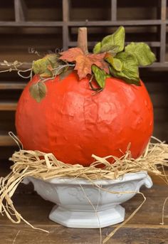 a large red pumpkin sitting on top of a white bowl filled with hay and leaves