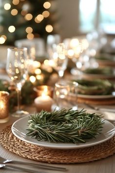 a table set for christmas dinner with greenery on the plate and candles in the background