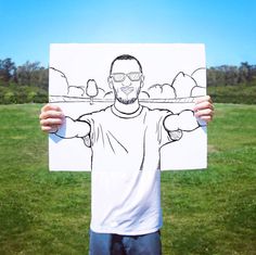 a man holding up a drawing of himself in front of the camera with his hands