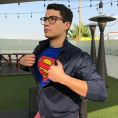 a man wearing a superman t - shirt while standing in front of a table and chairs