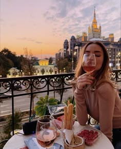 a woman sitting at an outdoor table drinking wine