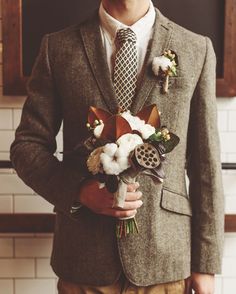 a man in a suit and tie with flowers on his lapel, standing against a wall