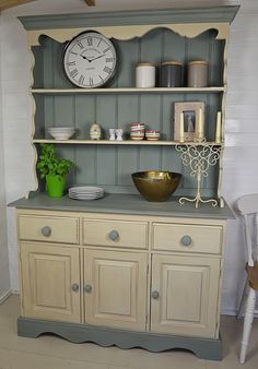 a white clock sitting on top of a wooden hutch next to a green plant