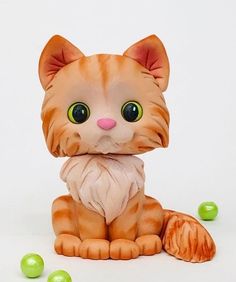 an orange and white cat figurine sitting next to some green balls on a white surface