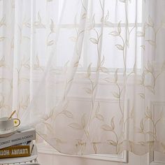 the curtains in this room are white and have gold leaves on them, along with a stack of books