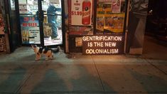 a small dog standing on the sidewalk in front of a building with signs and advertisements