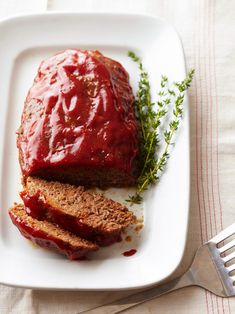 meatloaf with sauce and herbs on a white plate next to a silver fork