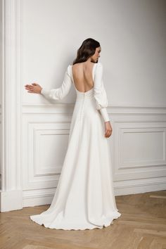 the back of a woman in a white wedding dress standing against a wall with her arms outstretched