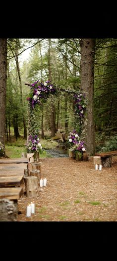 an outdoor ceremony setup with candles and flowers on the aisle, surrounded by trees in the woods