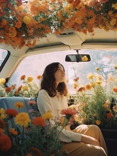 a woman sitting in the back seat of a car surrounded by flowers