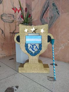 a wooden trophy with a blue and white stick in it's mouth sitting next to a potted plant